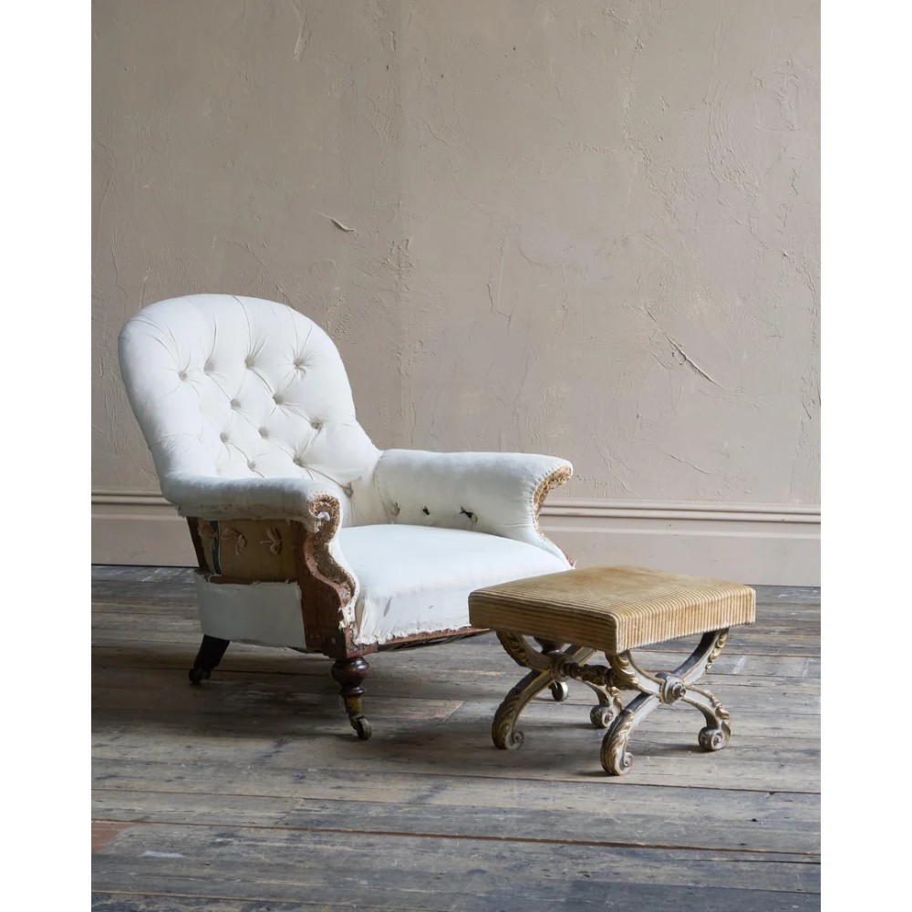 An antique curule X-frame footstool featuring carved scroll legs in grey paint and gilded finish with an upholstered top base. View IX