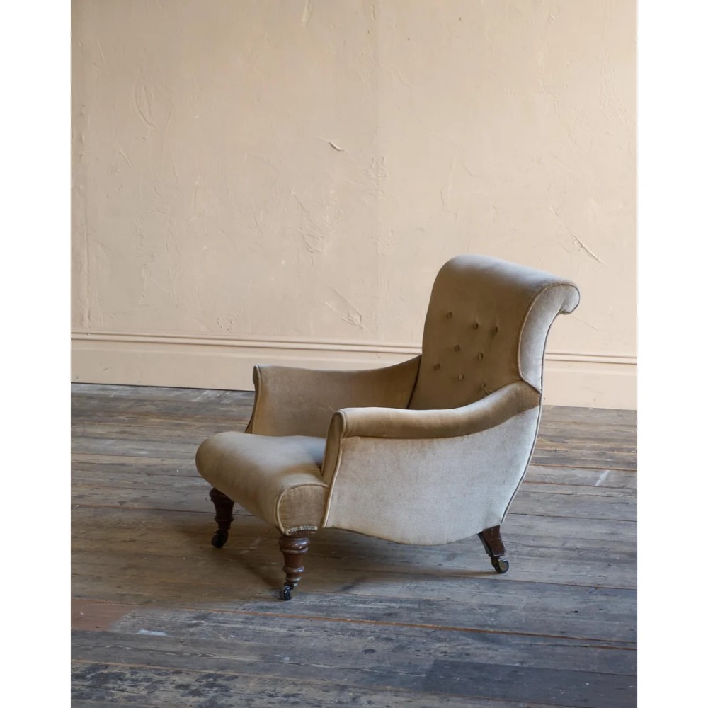 A Victorian button-back armchair upholstered in taupe velvet with turned front wooden legs set on metal castors.