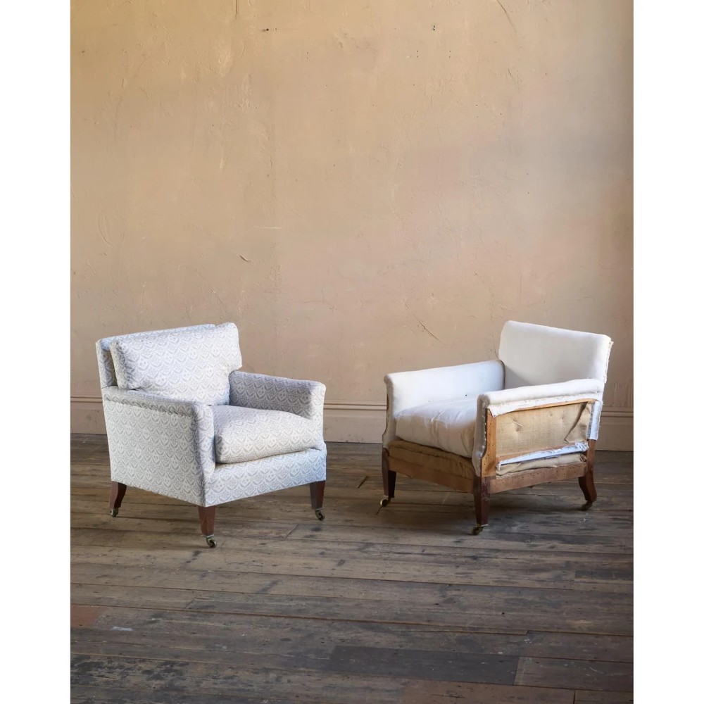 A pair of low-slung Victorian armchairs with turned wooden front legs and brass castors, one upholstered in patterned fabric and one in white calico.