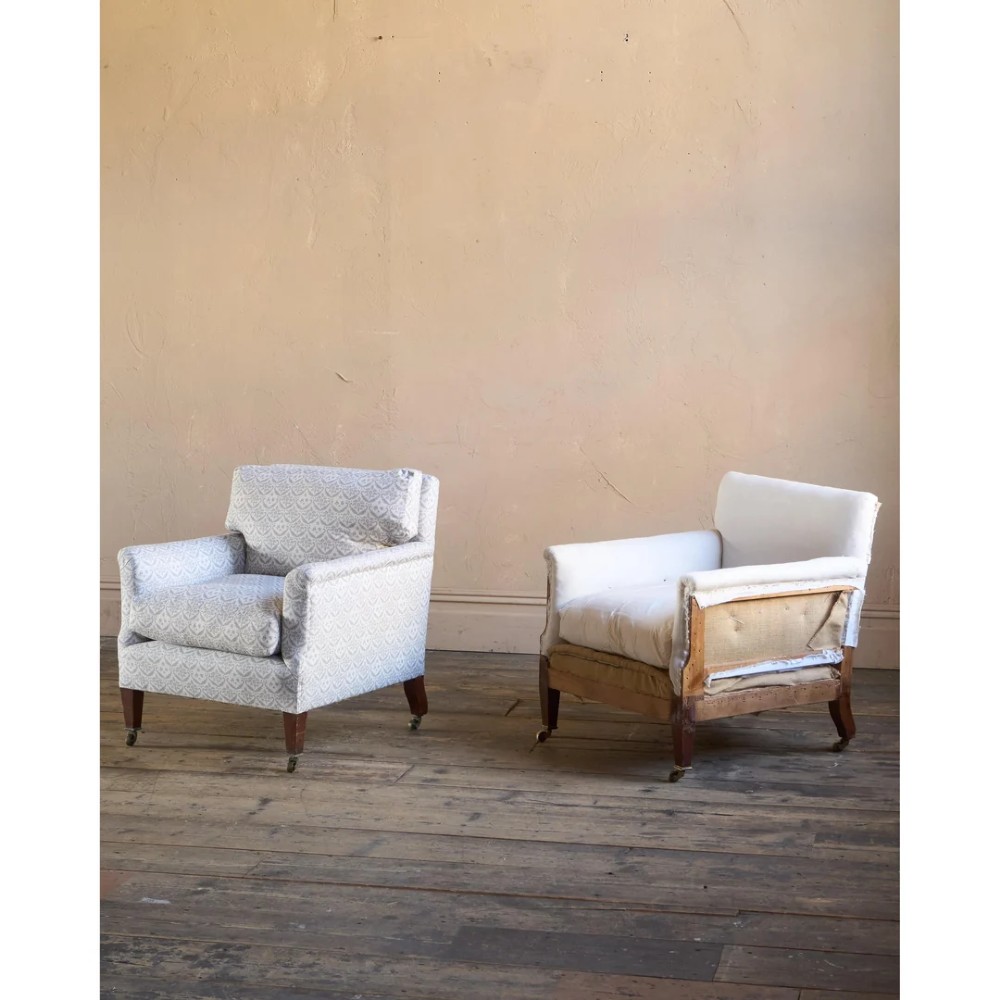 A pair of low-slung Victorian armchairs with turned wooden front legs and brass castors, one upholstered in patterned fabric and one in white calico. View II