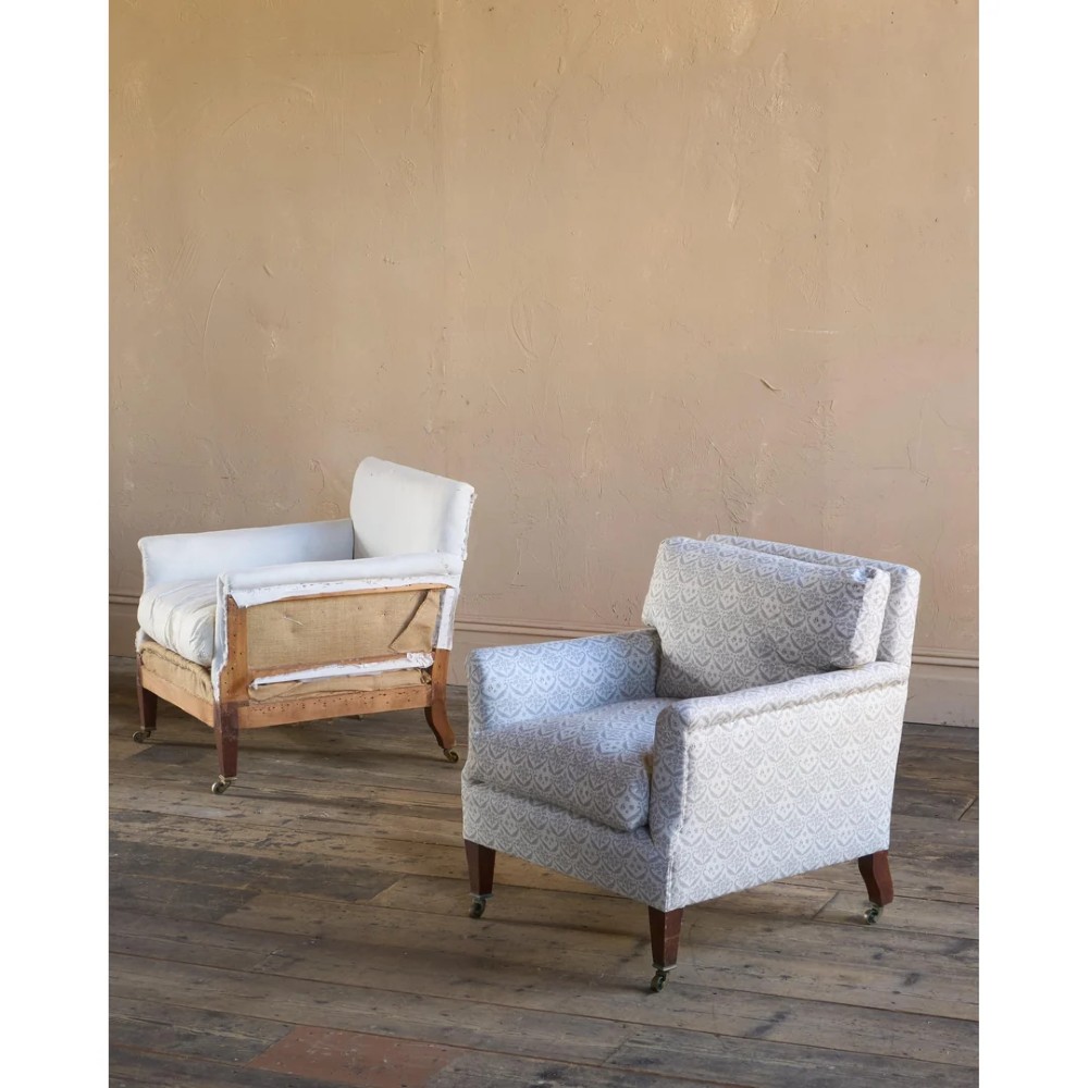A pair of low-slung Victorian armchairs with turned wooden front legs and brass castors, one upholstered in patterned fabric and one in white calico. View III