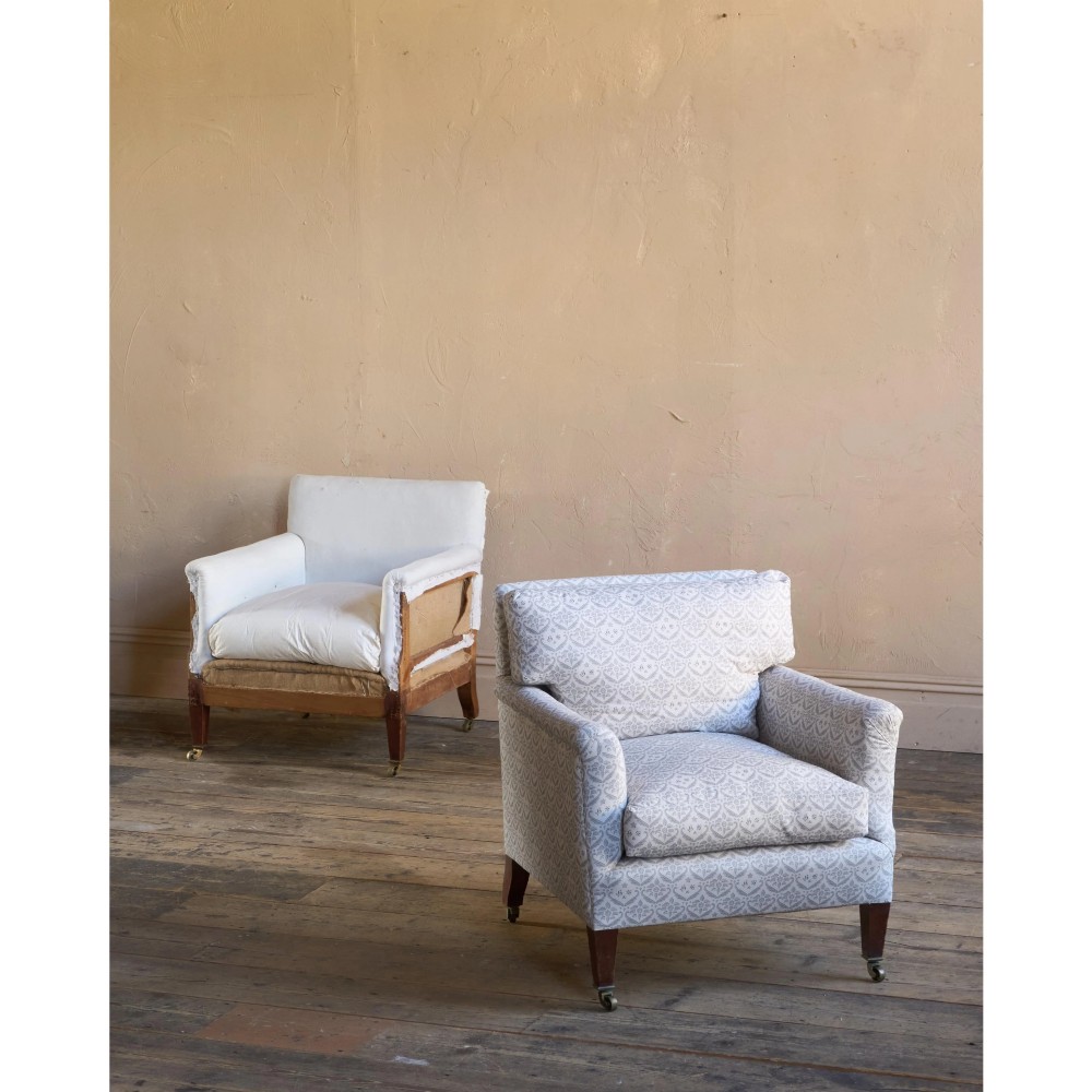 A pair of low-slung Victorian armchairs with turned wooden front legs and brass castors, one upholstered in patterned fabric and one in white calico. View IV