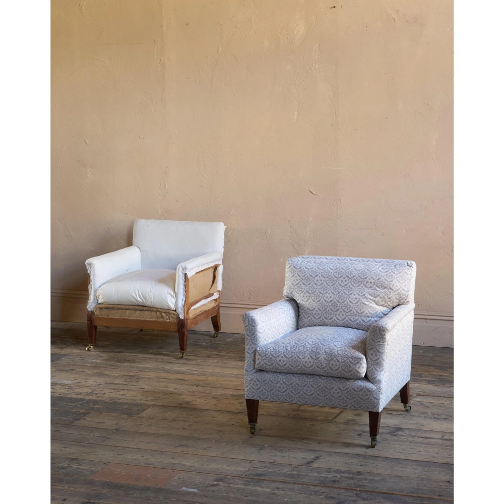 A pair of low-slung Victorian armchairs with turned wooden front legs and brass castors, one upholstered in patterned fabric and one in white calico. View V