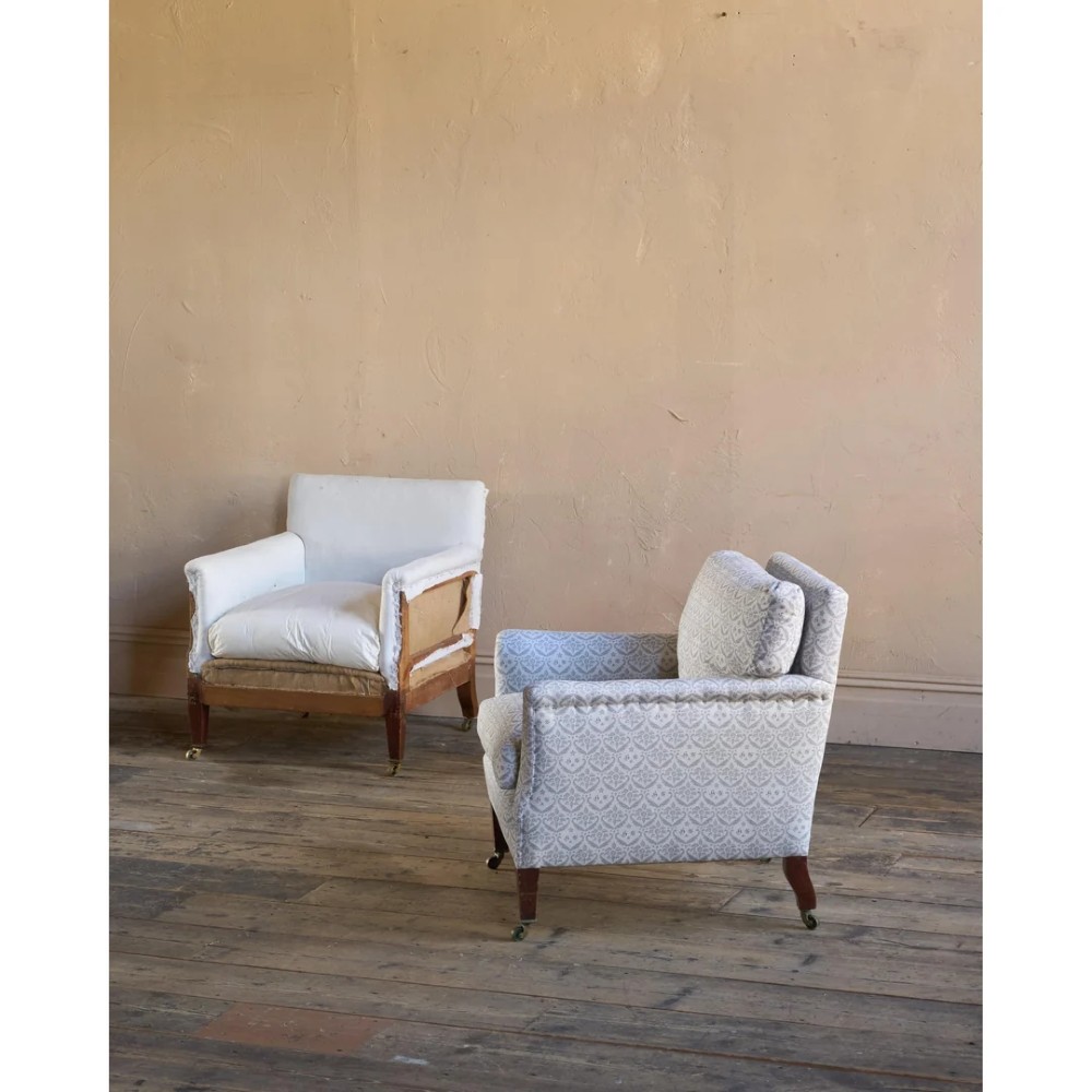A pair of low-slung Victorian armchairs with turned wooden front legs and brass castors, one upholstered in patterned fabric and one in white calico. View VI