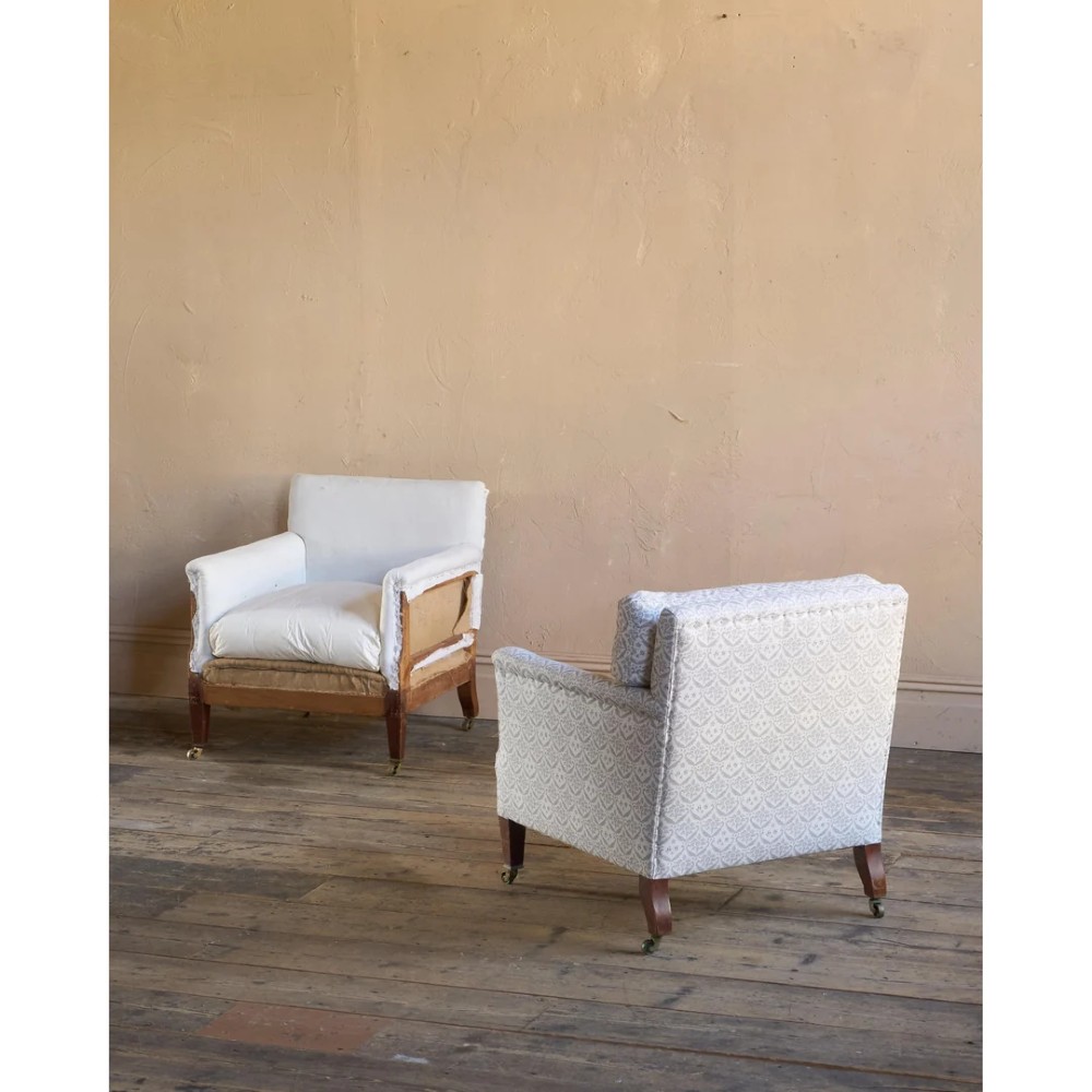 A pair of low-slung Victorian armchairs with turned wooden front legs and brass castors, one upholstered in patterned fabric and one in white calico. View VII