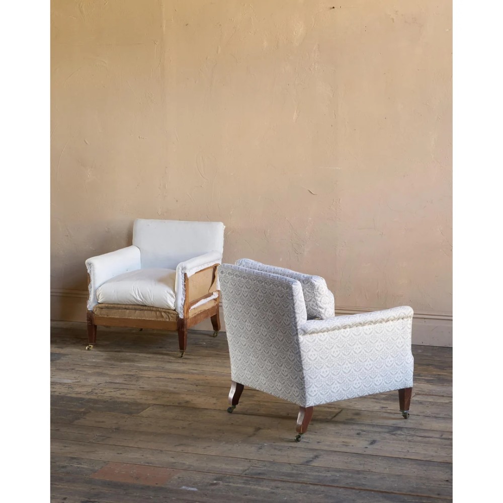 A pair of low-slung Victorian armchairs with turned wooden front legs and brass castors, one upholstered in patterned fabric and one in white calico. View VIII
