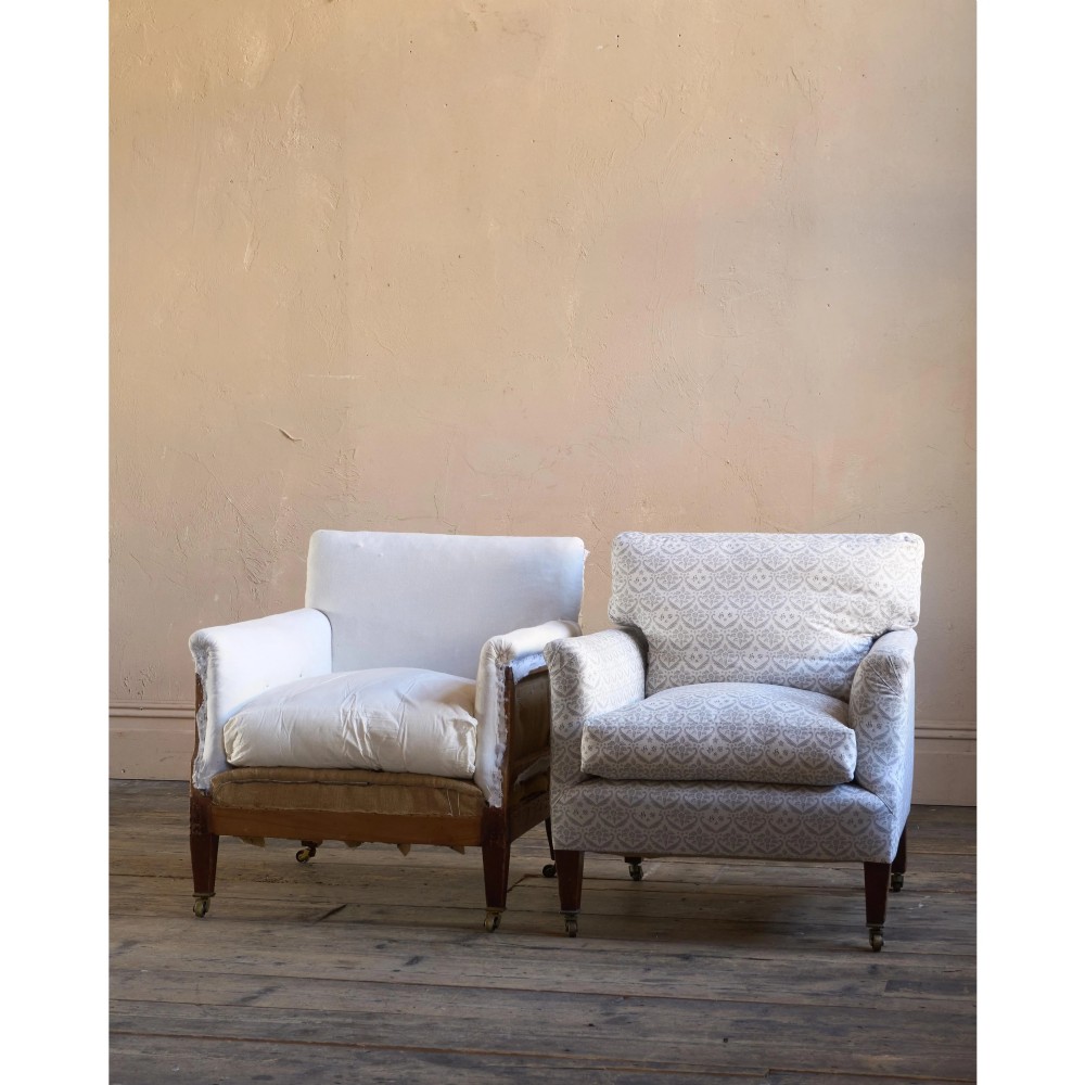 A pair of low-slung Victorian armchairs with turned wooden front legs and brass castors, one upholstered in patterned fabric and one in white calico. View X