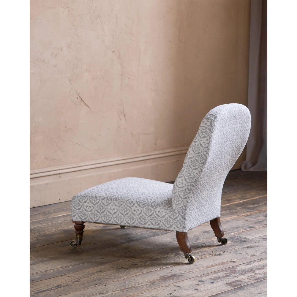 A low-seated Victorian armless slipper chair upholstered in grey patterned fabric with a button-back design and turned legs on brass castors. View III