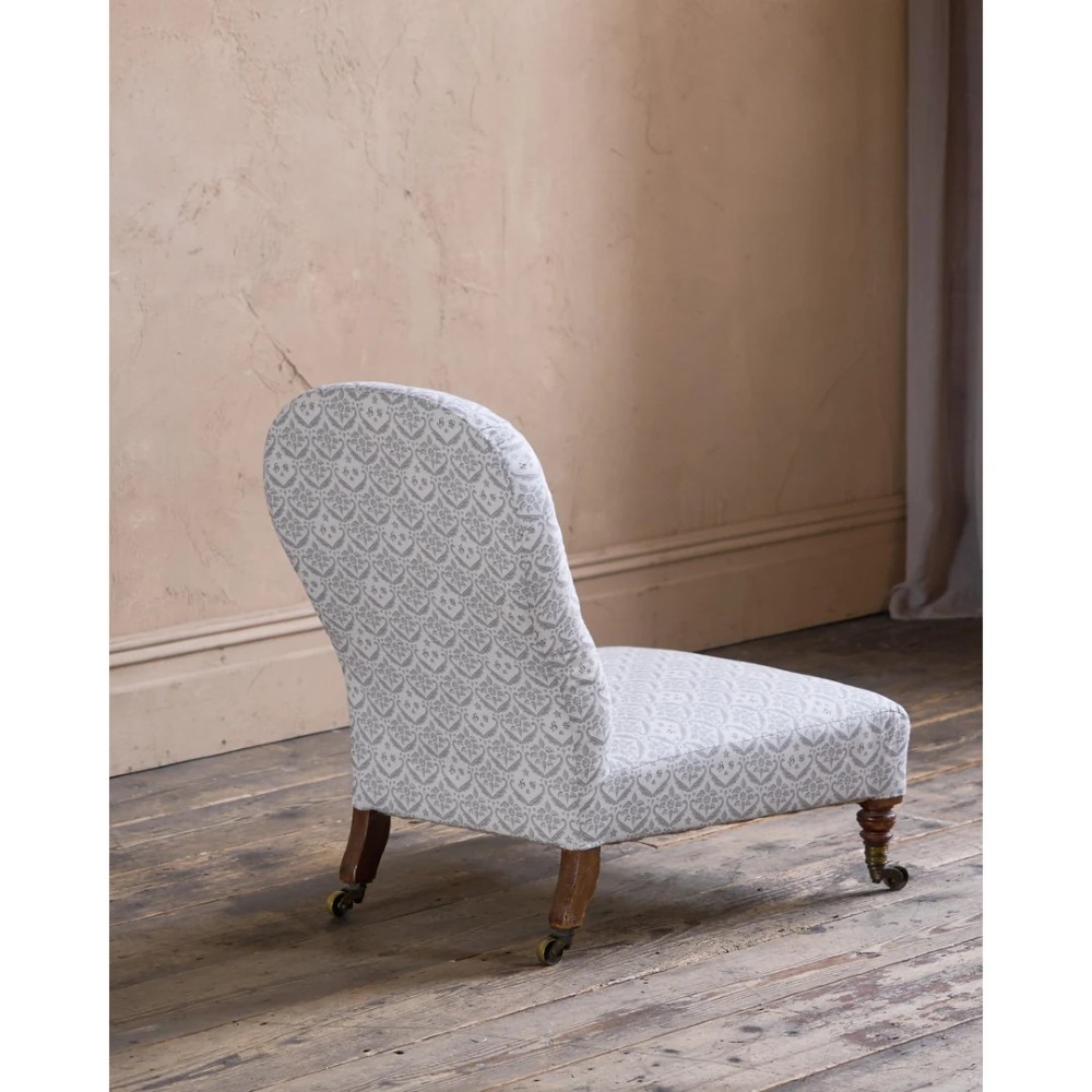 A low-seated Victorian armless slipper chair upholstered in grey patterned fabric with a button-back design and turned legs on brass castors. View IV
