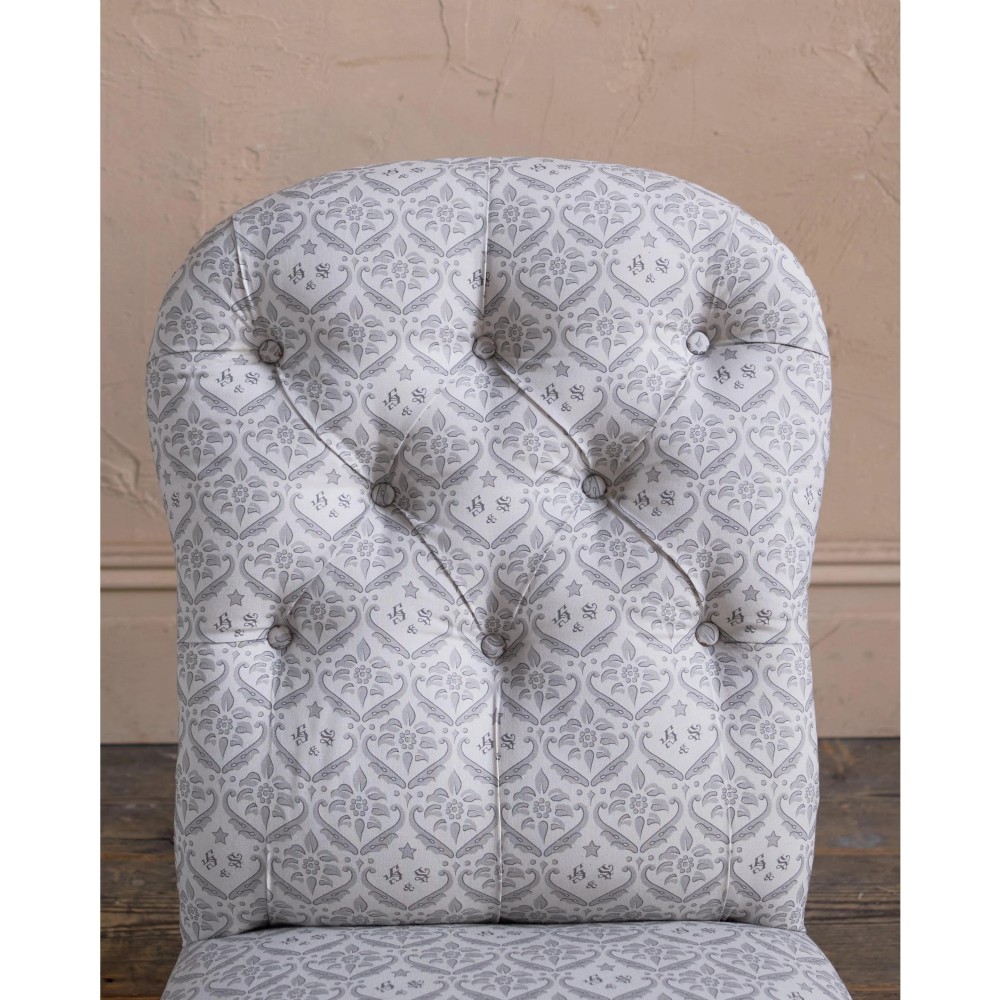 A low-seated Victorian armless slipper chair upholstered in grey patterned fabric with a button-back design and turned legs on brass castors. View V