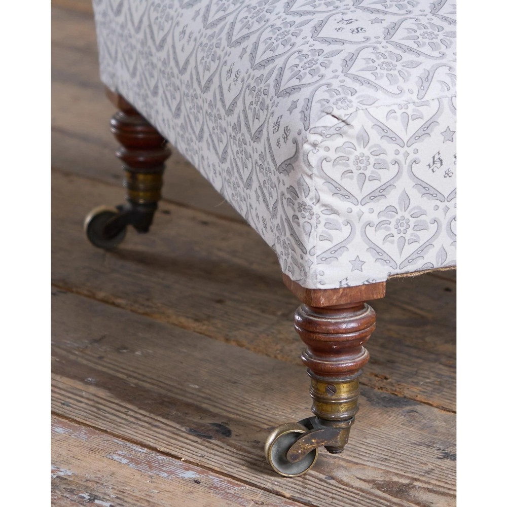 A low-seated Victorian armless slipper chair upholstered in grey patterned fabric with a button-back design and turned legs on brass castors. View VI