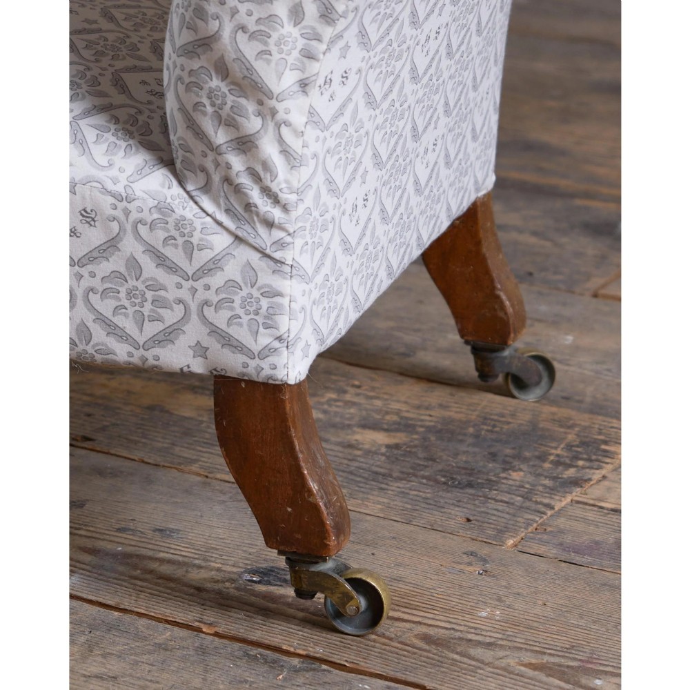 A low-seated Victorian armless slipper chair upholstered in grey patterned fabric with a button-back design and turned legs on brass castors. View VII