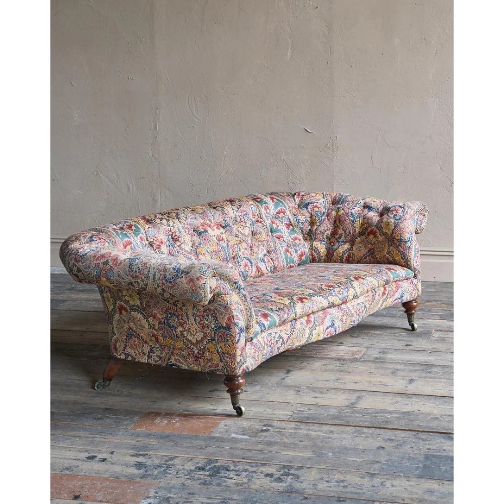 A Victorian Chesterfield sofa featuring deep-buttoned floral pattern upholstery, rolled arms, and turned wooden legs fitted with brass castors.