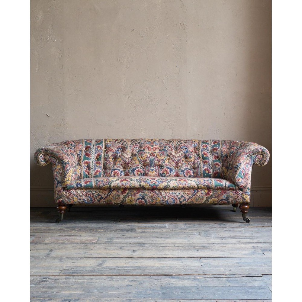 A Victorian Chesterfield sofa featuring deep-buttoned floral pattern upholstery, rolled arms, and turned wooden legs fitted with brass castors. View IV