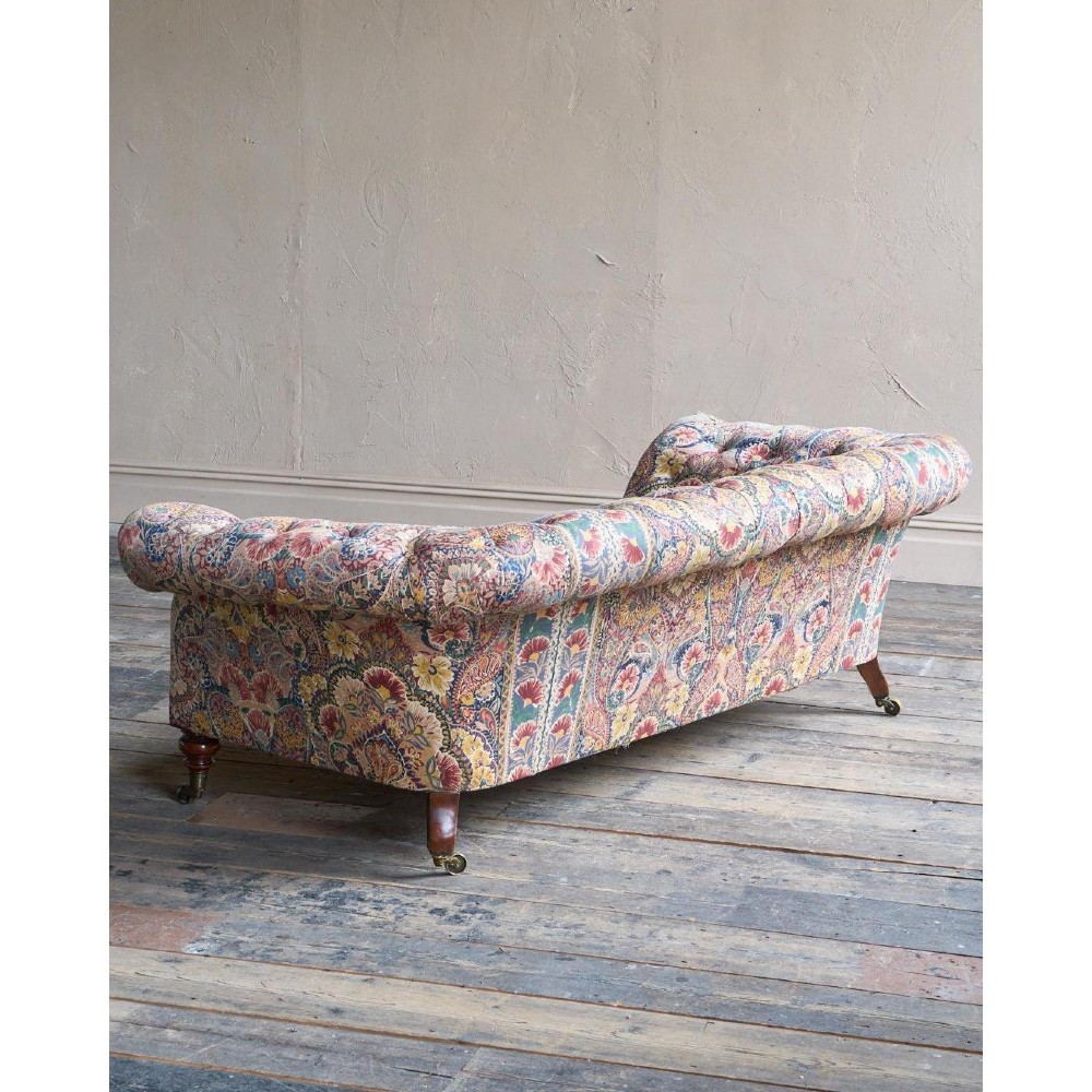 A Victorian Chesterfield sofa featuring deep-buttoned floral pattern upholstery, rolled arms, and turned wooden legs fitted with brass castors. View V