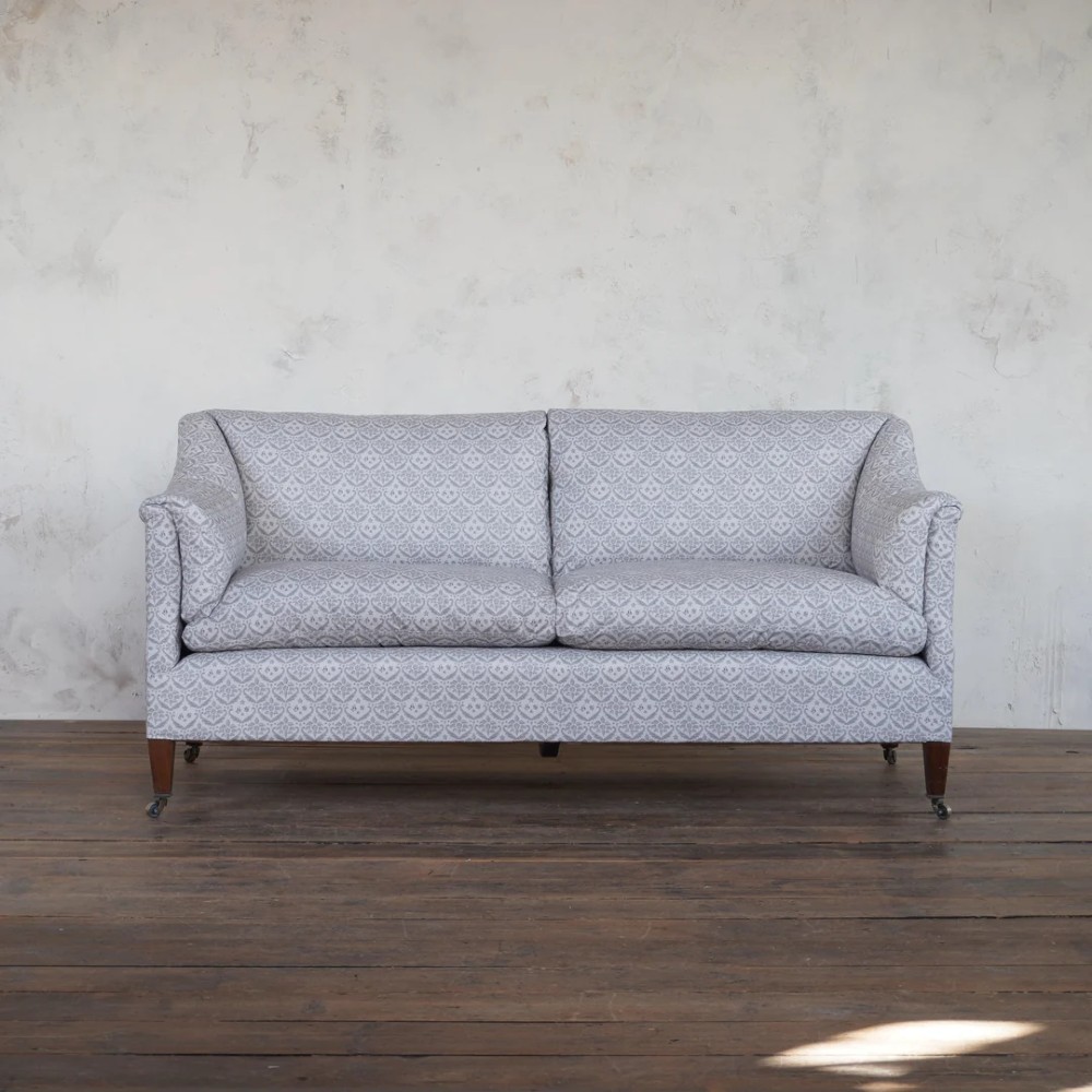 A two-seater Howard style sofa with sloped arms, grey geometric patterned upholstery, turned timber front legs, and brass castors. View II