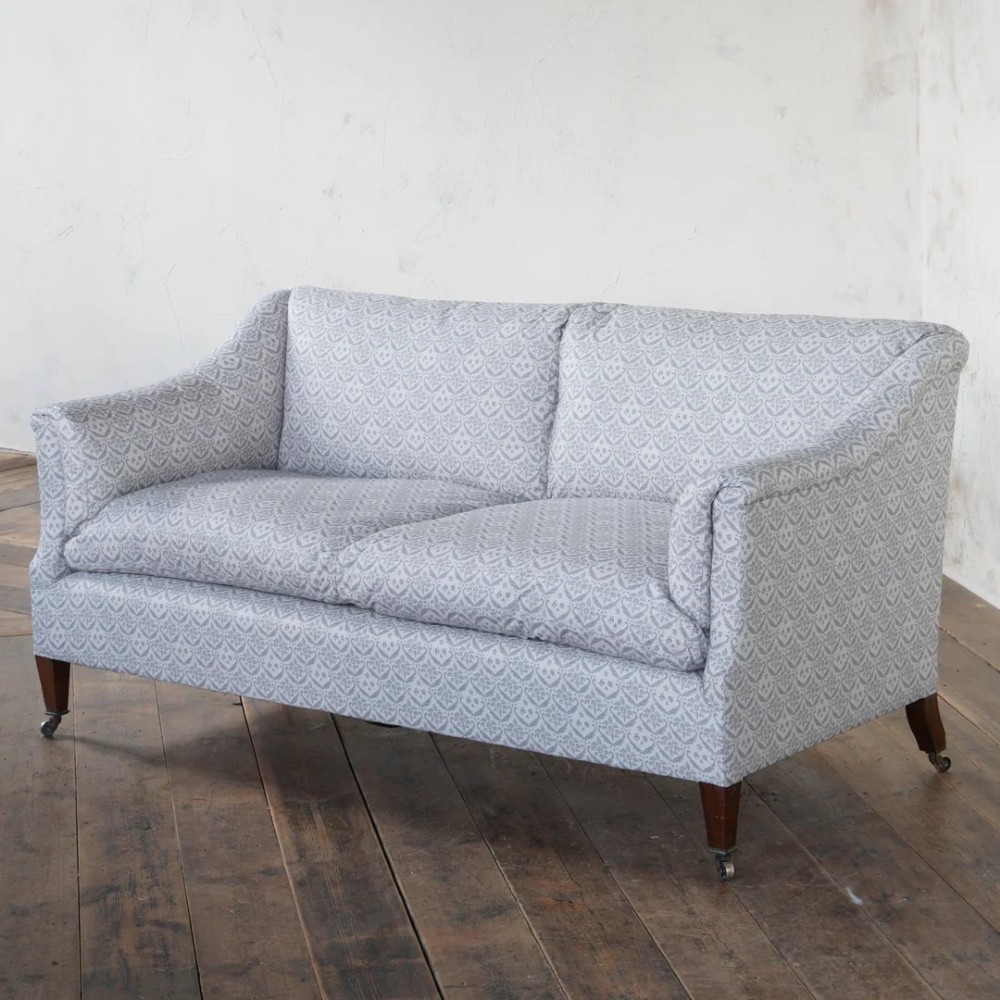 A two-seater Howard style sofa with sloped arms, grey geometric patterned upholstery, turned timber front legs, and brass castors. View III