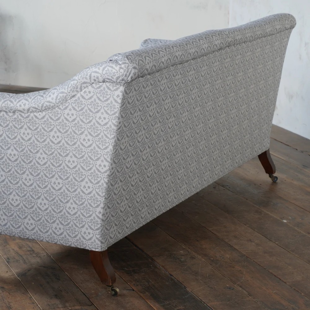 A two-seater Howard style sofa with sloped arms, grey geometric patterned upholstery, turned timber front legs, and brass castors. View IV