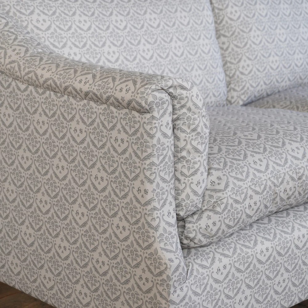 A two-seater Howard style sofa with sloped arms, grey geometric patterned upholstery, turned timber front legs, and brass castors. View V