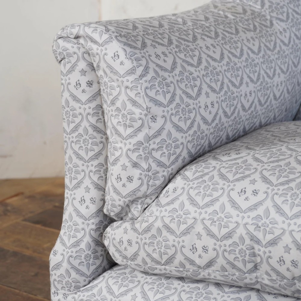 A two-seater Howard style sofa with sloped arms, grey geometric patterned upholstery, turned timber front legs, and brass castors. View VI