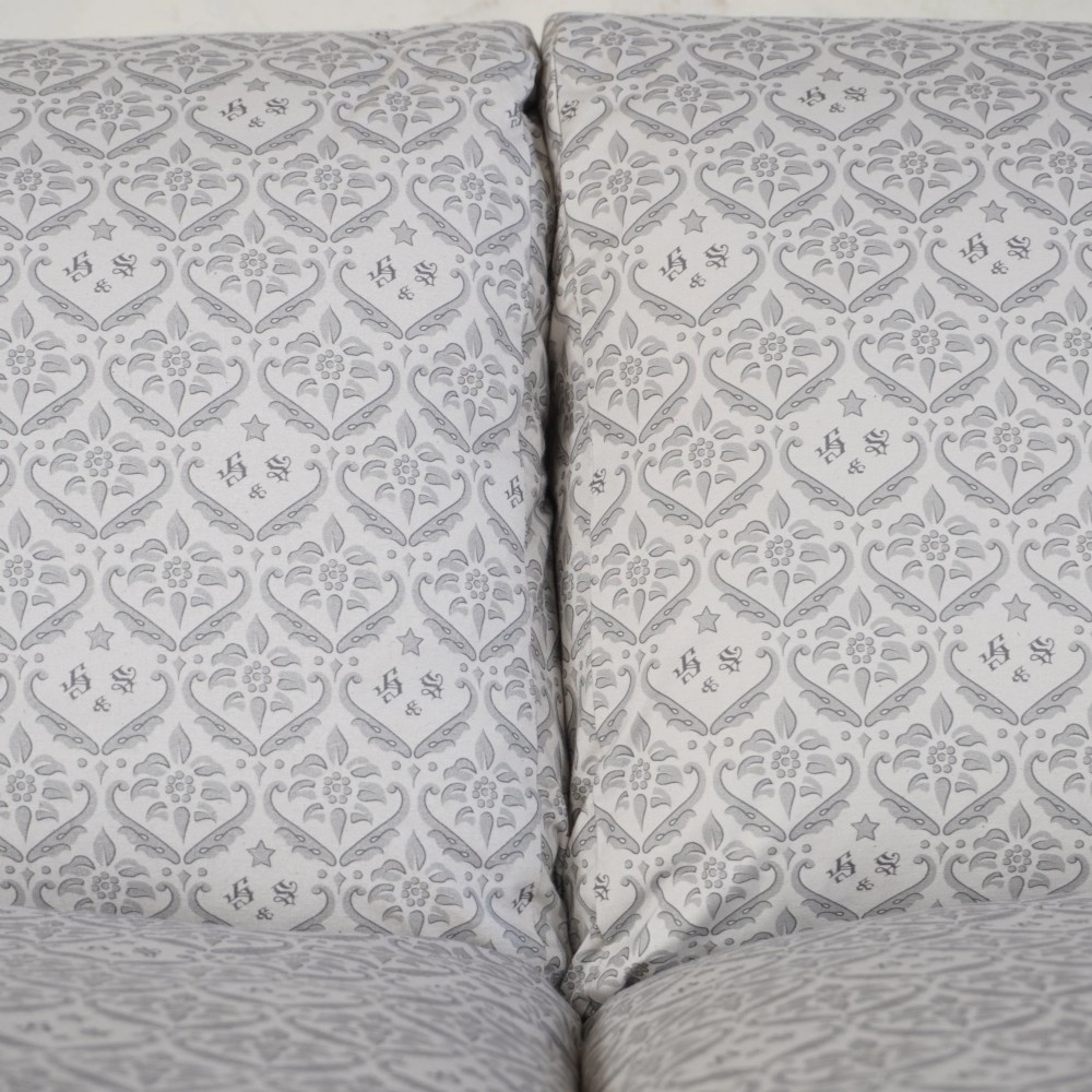 A two-seater Howard style sofa with sloped arms, grey geometric patterned upholstery, turned timber front legs, and brass castors. View VII