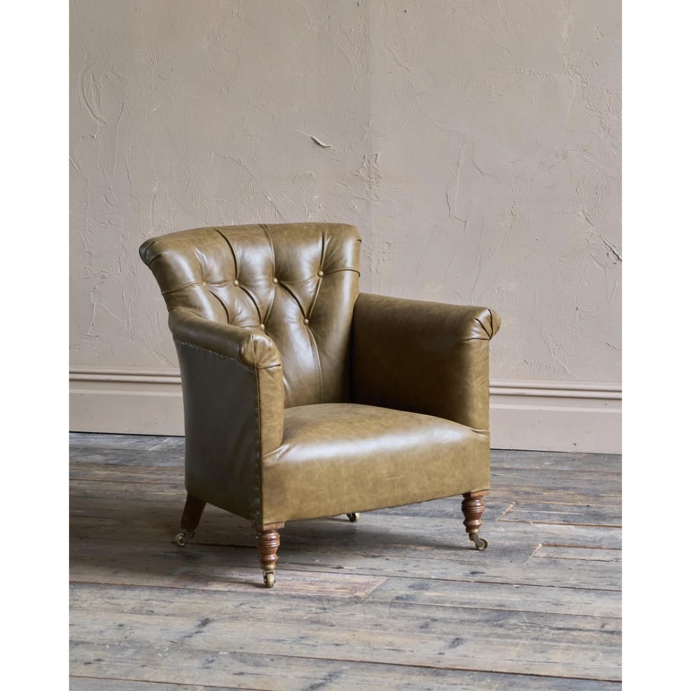 A deep-buttoned olive green leather armchair featuring turned wooden front legs with brass castors.