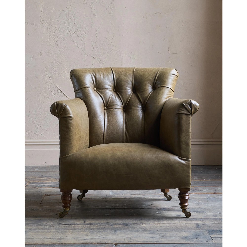 A deep-buttoned olive green leather armchair featuring turned wooden front legs with brass castors. View II