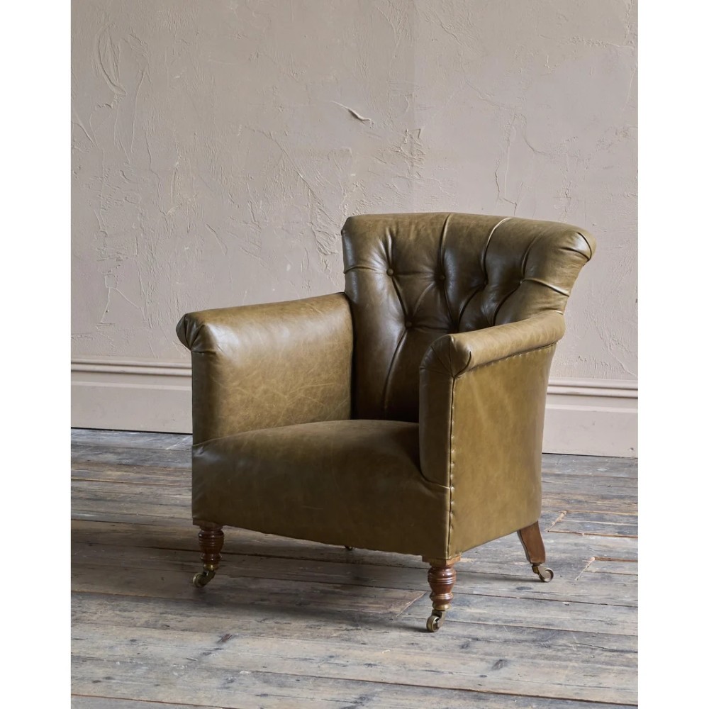 A deep-buttoned olive green leather armchair featuring turned wooden front legs with brass castors. View III