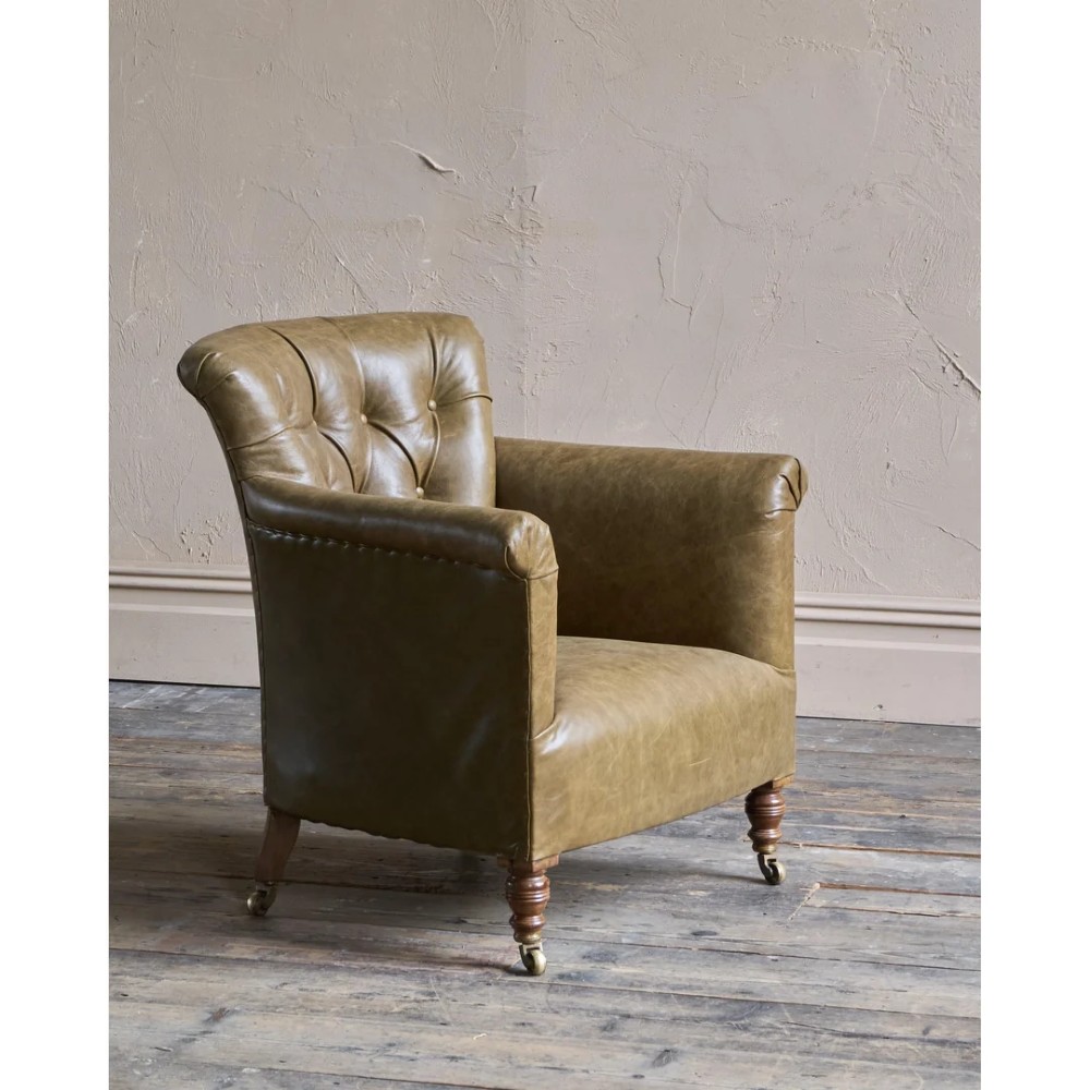 A deep-buttoned olive green leather armchair featuring turned wooden front legs with brass castors. View IV