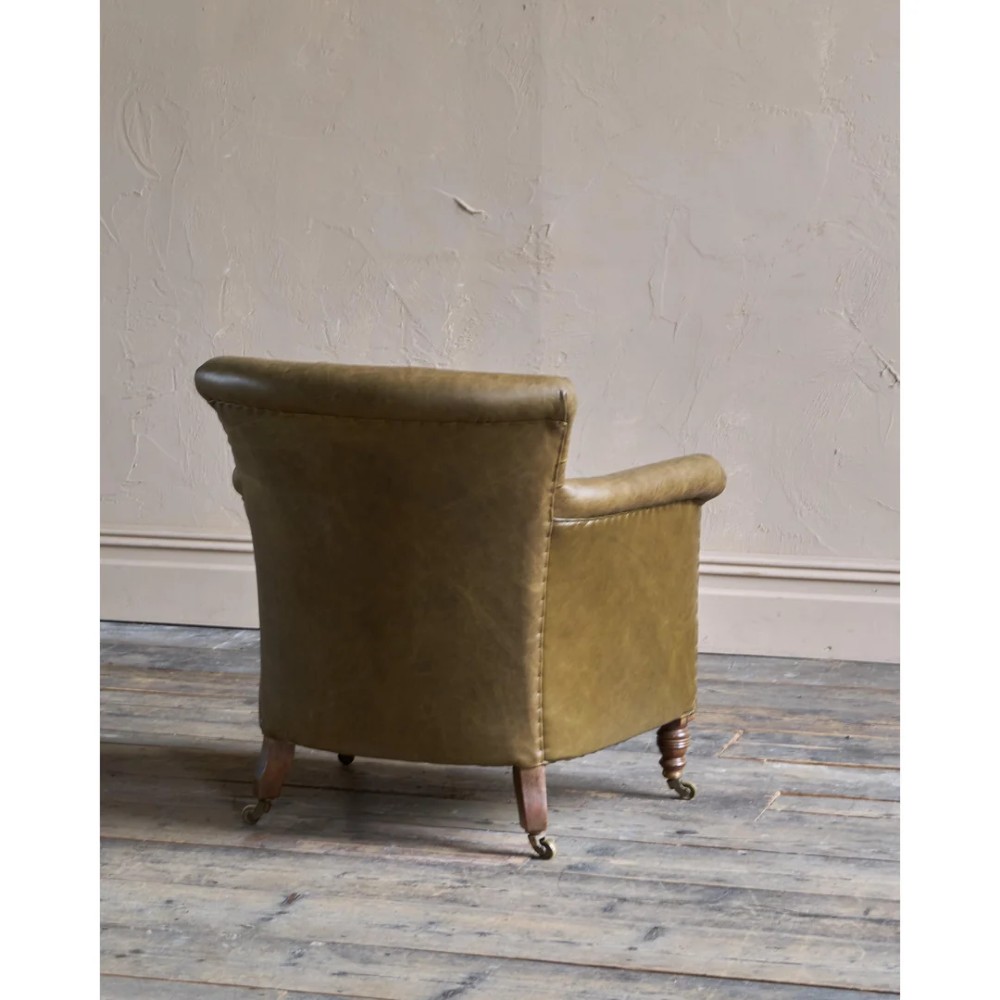 A deep-buttoned olive green leather armchair featuring turned wooden front legs with brass castors. View V