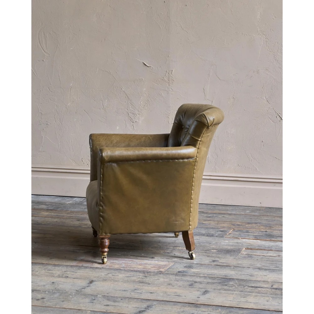 A deep-buttoned olive green leather armchair featuring turned wooden front legs with brass castors. View VI