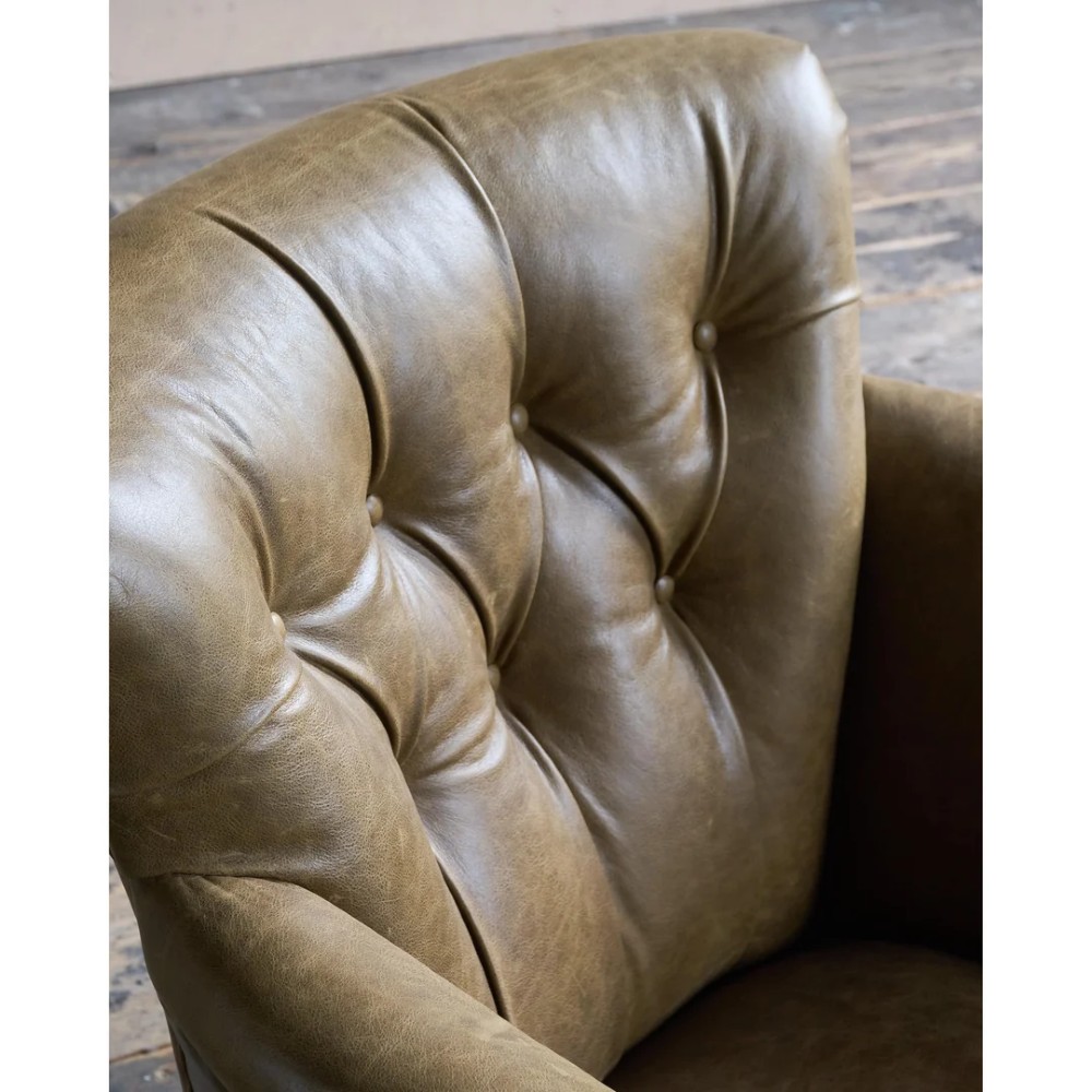 A deep-buttoned olive green leather armchair featuring turned wooden front legs with brass castors. View VII