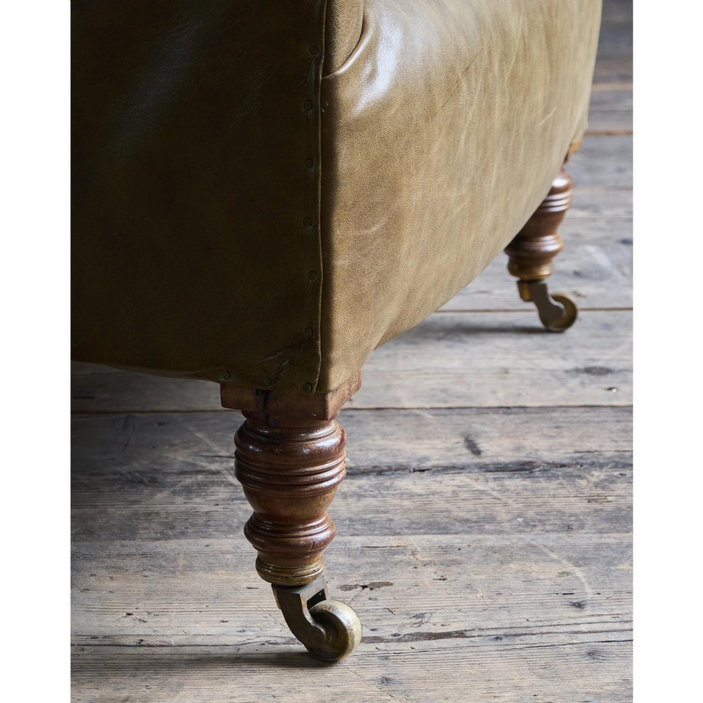A deep-buttoned olive green leather armchair featuring turned wooden front legs with brass castors. View VIII
