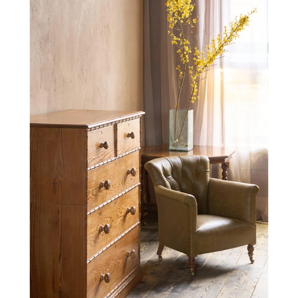 A deep-buttoned olive green leather armchair featuring turned wooden front legs with brass castors. View XIII