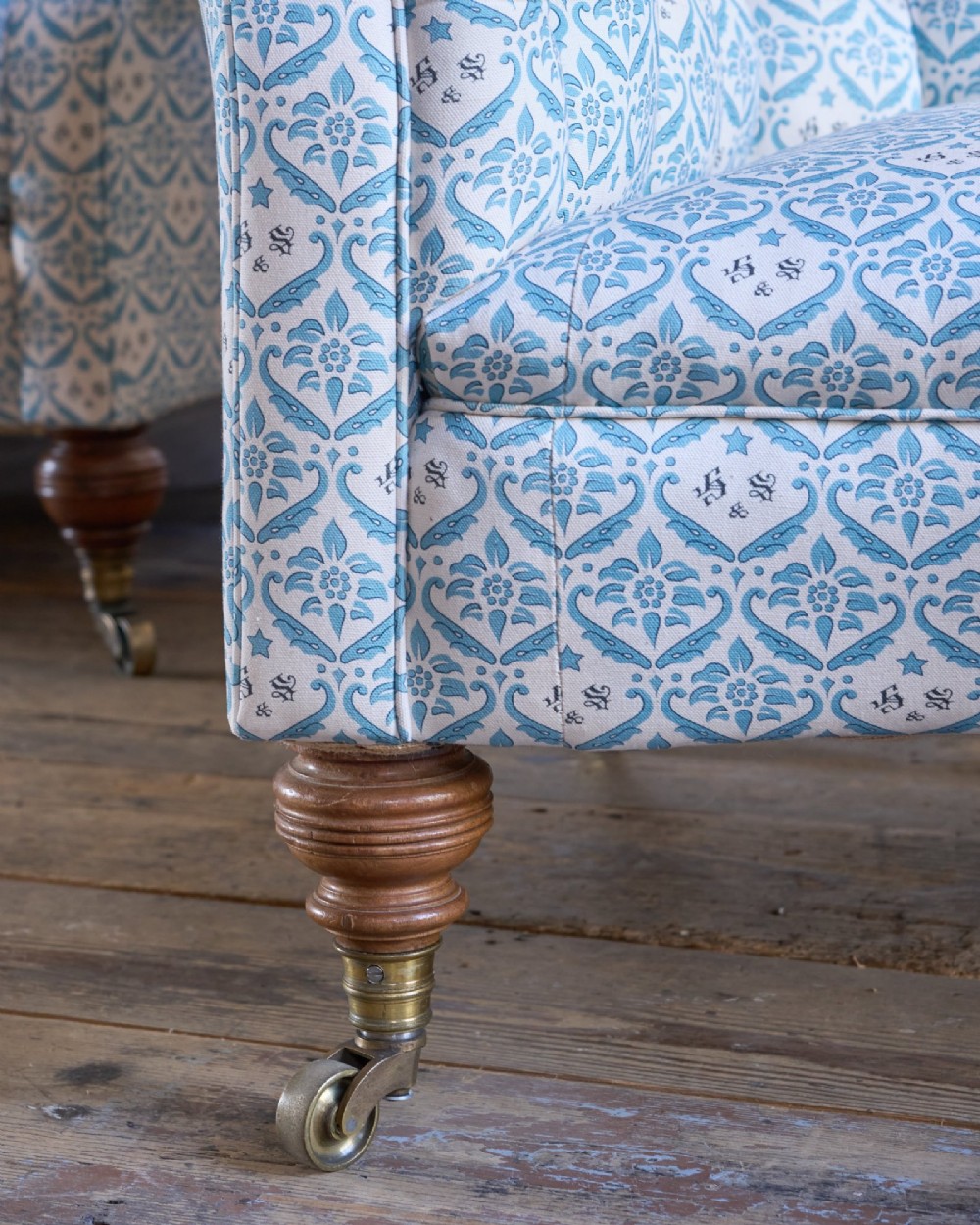 A pair of antique serpentine Chesterfield sofas featuring light blue patterned fabric, deep button-tufted backrests, rolled arms, and turned wooden legs on brass castors. View VI