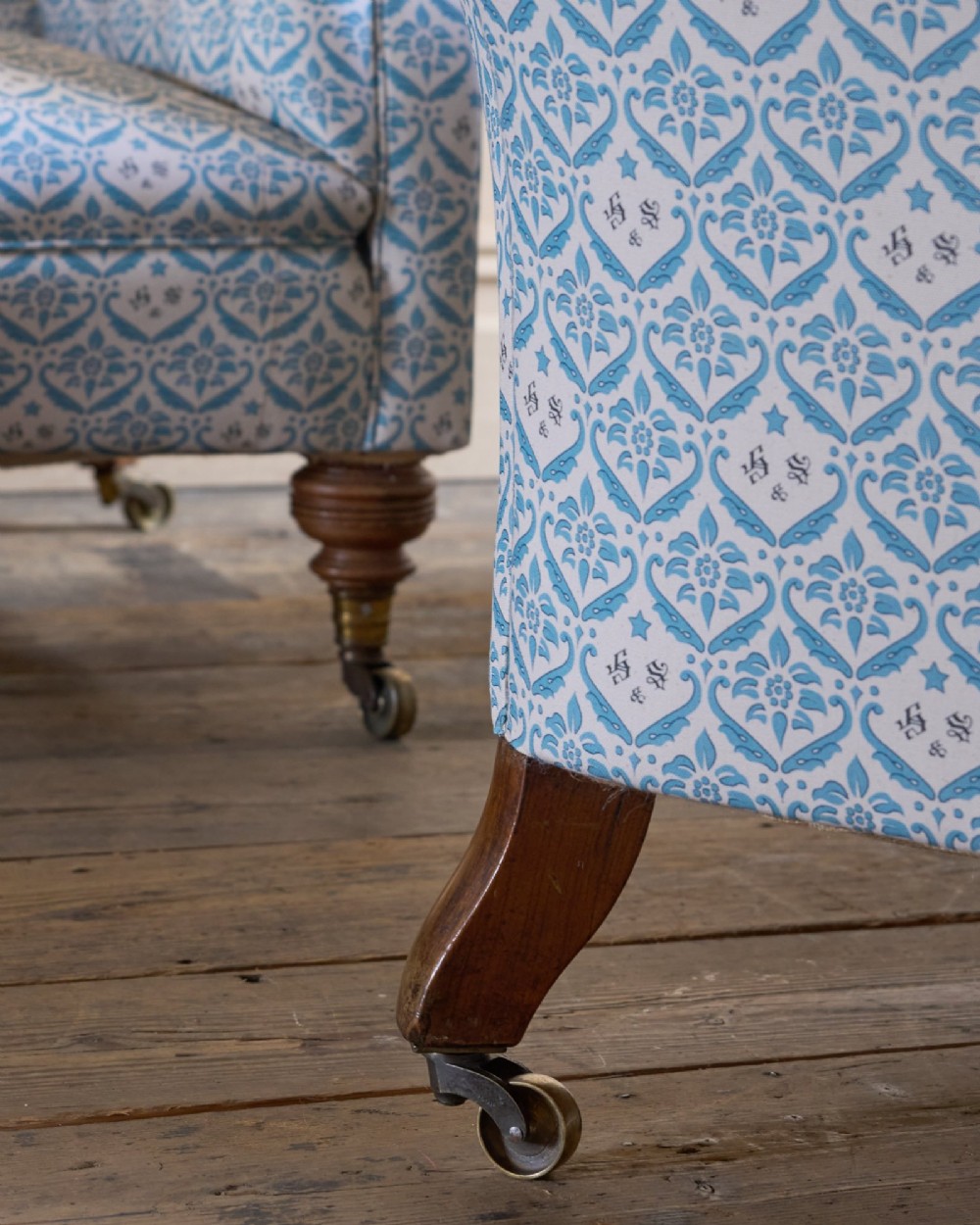 A pair of antique serpentine Chesterfield sofas featuring light blue patterned fabric, deep button-tufted backrests, rolled arms, and turned wooden legs on brass castors. View XI