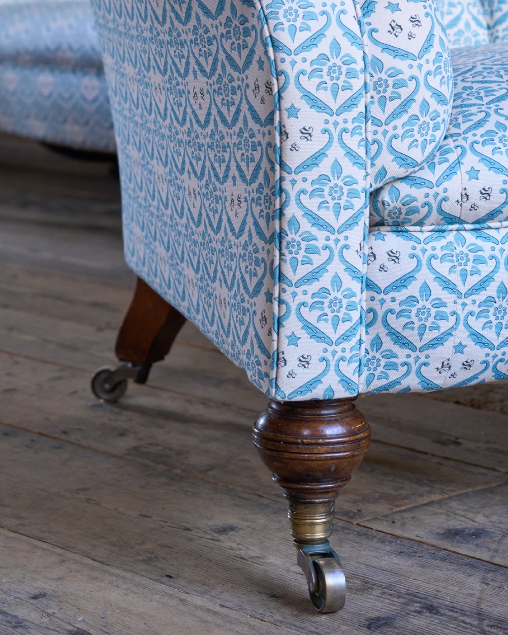 A pair of antique serpentine Chesterfield sofas featuring light blue patterned fabric, deep button-tufted backrests, rolled arms, and turned wooden legs on brass castors. View XII