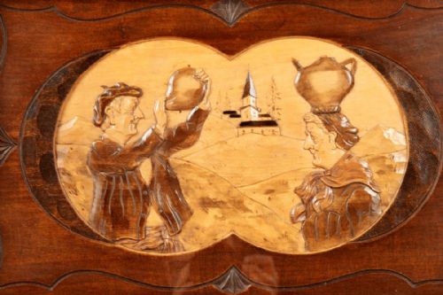 fig 1. A rectangular warm brown carved wooden tray featuring stylized Art Deco ribbed handles and a central inlaid relief scene of two figures and a village church.