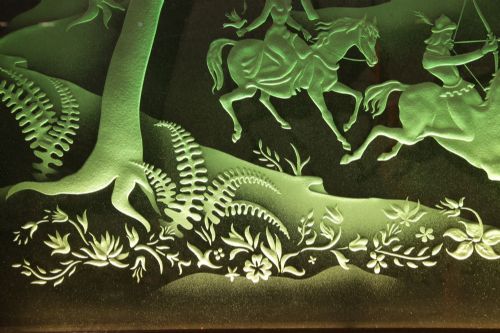 fig 2. A large rectangular dark wood frame housing an illuminated green sandblasted glass panel featuring a detailed hunting scene with horseback archers, hounds, stags, and a castle.