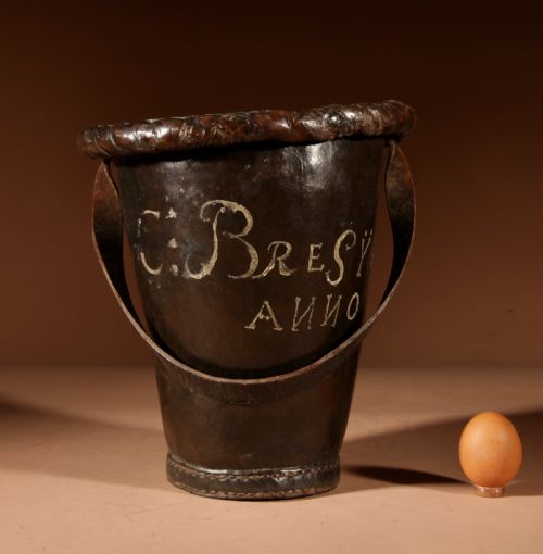 fig 1. An 18th-century dark brown leather fire bucket featuring a tall stitched leather handle, a thick rolled rim, and hand-painted cream lettering reading BRESYL ANNO 1776.