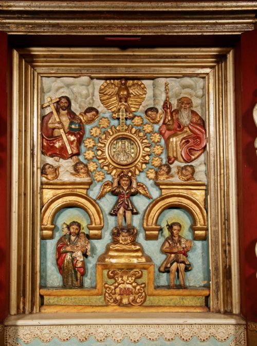 fig 1. A polychrome wooden Spanish home altar with open red doors featuring carved saint figurines surrounding a gilded central shrine.