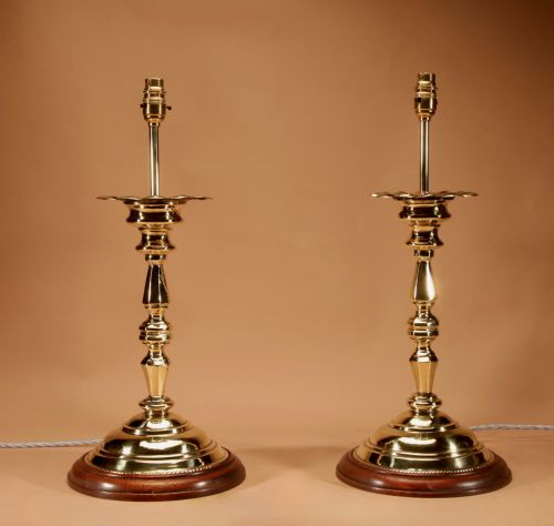 fig 1. A pair of turned brass candlestick-style table lamps set on circular wooden bases with cream pleated shades.