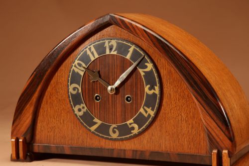 fig 1. An Amsterdam School mantel clock featuring an arched oak case framed with dark Macassar ebony trim and a circular dial with brass numbers.