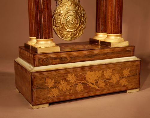 fig 2. An antique rosewood portico clock with four fluted columns, gilt ormolu capitals, floral lemonwood marquetry inlays, and an exposed pendulum.
