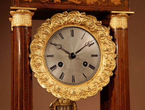 fig 3. An antique rosewood portico clock with four fluted columns, gilt ormolu capitals, floral lemonwood marquetry inlays, and an exposed pendulum.