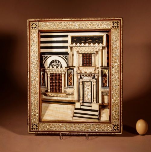 fig 1. A framed three-dimensional wooden relief diorama depicting a Moorish building facade with intricate mother-of-pearl geometric inlay, miniature lattice windows, and Arabic calligraphy.