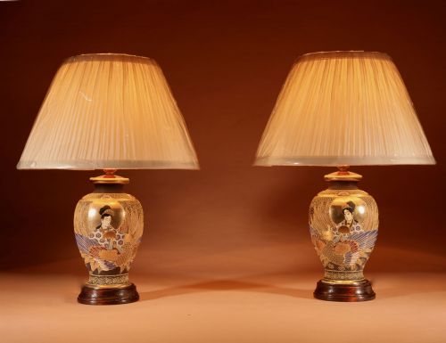 fig 1. A pair of small Japanese Satsuma ceramic table lamps featuring figure paintings, gold gilding, dark wooden bases, and pleated cream shades.