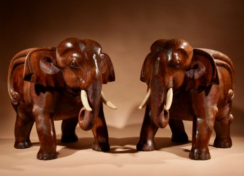 fig 1. A pair of heavy hand-carved wooden armchairs sculpted in the form of standing elephants with textured hides and light-coloured tusks.