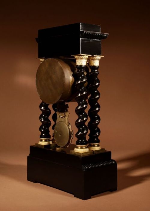 An ebonised French portico clock featuring brass stringing inlay, four barley-twist columns, an ornate gilt dial bezel, and an exposed ornate pendulum. View III