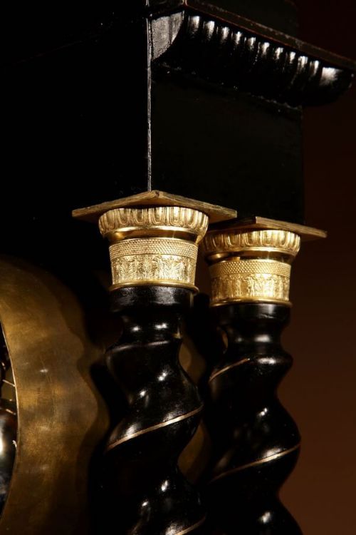 An ebonised French portico clock featuring brass stringing inlay, four barley-twist columns, an ornate gilt dial bezel, and an exposed ornate pendulum. View VI